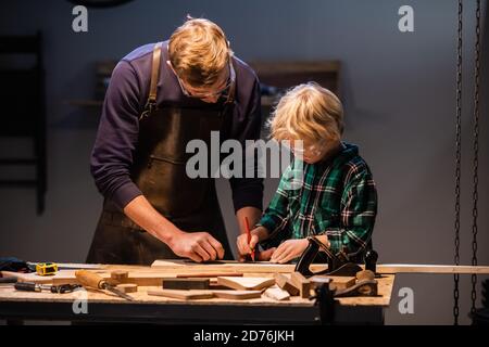 un giovane padre e il suo figliolo fanno un giocattolo di legno in un laboratorio di falegname Foto Stock