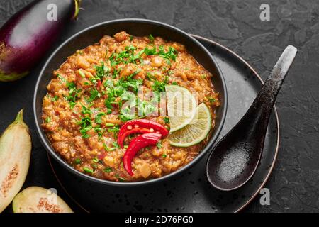 Baingan Bharta o purea arrosto Eggplant in ciotola nera su tavolo di ardesia scuro. Bhurta è un piatto di purea di cucina indiana con melanzane arrostite al fuoco e masa Foto Stock