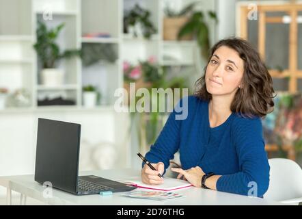 Una giovane donna bruna usa un computer portatile in ufficio o a casa. Foto Stock