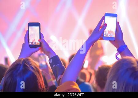 Gli adolescenti scattano foto o registrano video di concerti di musica dal vivo con lo smartphone. Illuminazione da palco colorata e luminosa. Vita notturna, tecnologia, fotografia Foto Stock