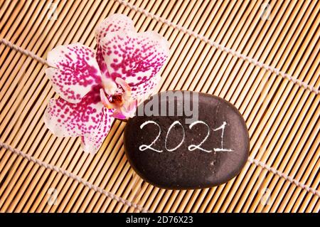 2021 scritto su un ciottolo nero con orchidea rosa, zen biglietto di auguri per il nuovo anno Foto Stock
