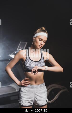 Giovane sportivo in auricolari che guarda l'orologio intelligente in palestra Foto Stock