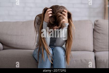 Disperata giovane donna seduta testa in mani sul divano e piangendo, panorama Foto Stock