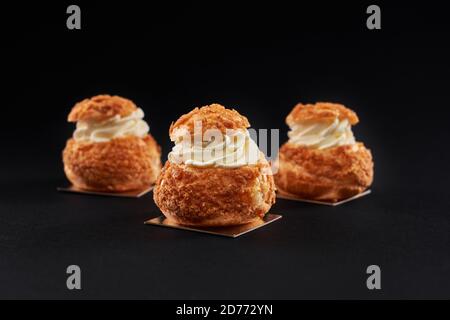 Vista in primo piano di deliziosi profiteroles freschi con crema bianca dolce all'interno. Eclair gustosi fatti in casa isolati su sfondo nero studio. Concetto di dessert, cibo da ristorante. Foto Stock