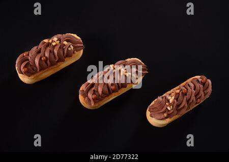 Biscotti frollini con panna di cioccolato marrone montata con mascarpone. Vista dall'alto di tre dolci freschi fatti in casa isolati su sfondo nero. Concetto di dolci, industria alimentare. Foto Stock