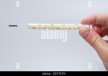 termometro a mercurio isolato sulla mano dell'uomo su sfondo blu.  Misurazione della temperatura mediante un termometro. Febbre alta e  malattia. Primo piano Foto stock - Alamy