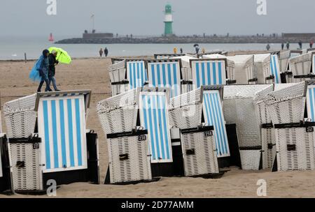 21 ottobre 2020, Meclemburgo-Pomerania occidentale, Warnemünde: Sulla spiaggia del Mar Baltico, gli escursionisti camminano con ombrelloni sotto la pioggia, le sedie a sdraio sono pronte per il trasporto. Foto: Bernd Wüstneck/dpa-Zentralbild/dpa Foto Stock