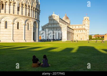 I turisti si siedono sull'erba di fronte al Battistero di San Giovanni a Pisa, Toscana, Italia Foto Stock