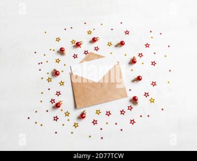 Carta vuota su busta del mestiere e varie decorazioni di natale su texture sfondo bianco mockup di festa e invito. Vista dall'alto. Foto Stock