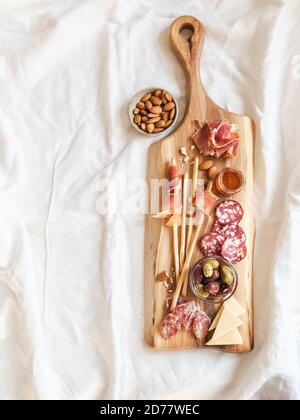 Tavolo per spuntini. Varietà di salsiccia, olive, formaggio, bastoncini di pane, su tagliere di legno su una tovaglia bianca. Disposizione piatta. Vista dall'alto. Spazio di copia Foto Stock