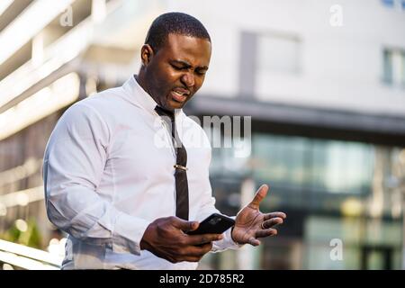 Ritratto di un uomo d'affari afro-americano frustrato che utilizza lo smartphone. Foto Stock