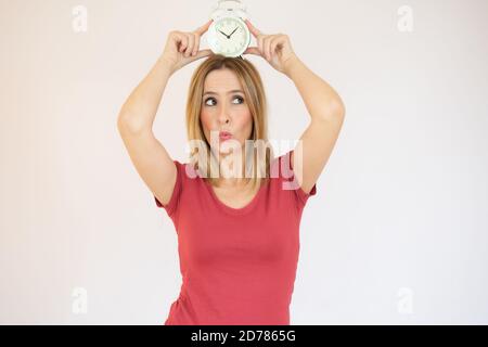 Guarda il concetto di tempo. La donna sta tenendo una sveglia sopra la testa. Giovane donna attraente con orologio isolato su sfondo bianco. Tieni traccia Foto Stock