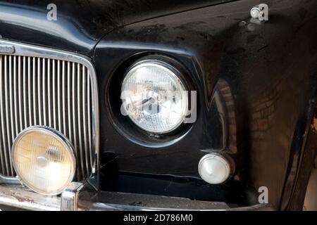 bianco e nero, immagine ravvicinata di fari per auto d'epoca classici di lusso neri, luce spot e griglia parcheggiati. Veicolo vecchio non in uso con polvere su bo Foto Stock