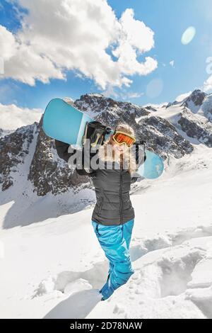 Bella giovane donna snowboarder va in per gli sport invernali in montagne innevate si erge nella neve e tiene uno snowboard Foto Stock