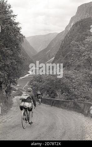 Anni '50, storico, cicloturistica sulle Alpi svizzere, due ciclisti maschili in bicicletta dell'epoca cavalcando una strada di montagna sassosa, con attrezzatura da campeggio attaccata. Foto Stock