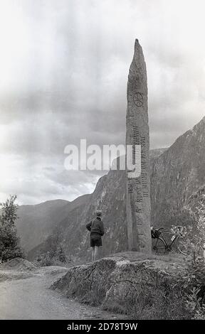 Anni '50, storico, cicloturando le Alpi svizzere, un ciclista maschile nelle Alpi che si trova accanto a una statua di pietra, dicendo 'Norsk Ungdom Seite...... Foto Stock