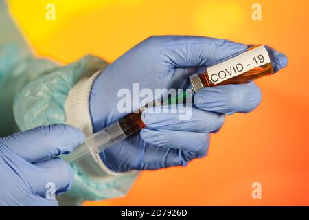 Un medico con guanti blu aspira una fiala in una siringa. Vaccino medico contro il concetto di influenza coronavirus flacone di iniezione per vetro medico Foto Stock