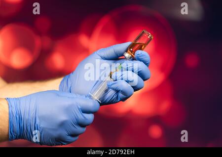 Un medico con guanti blu aspira una fiala in una siringa. Vaccino medico contro il concetto di influenza coronavirus flacone di iniezione per vetro medico Foto Stock