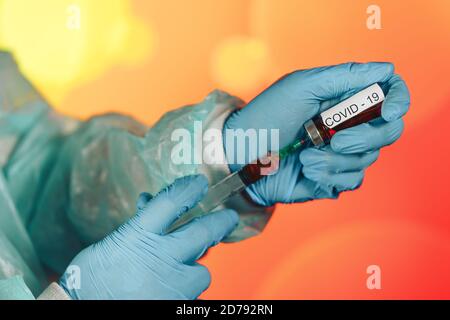 Un medico con guanti blu aspira una fiala in una siringa. Vaccino medico contro il concetto di influenza coronavirus flacone di iniezione per vetro medico Foto Stock