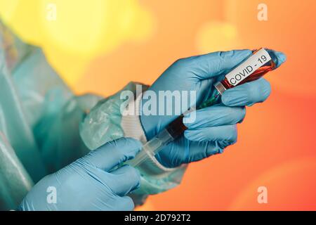 Un medico con guanti blu aspira una fiala in una siringa. Vaccino medico contro il concetto di influenza coronavirus flacone di iniezione per vetro medico Foto Stock
