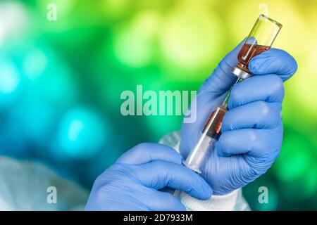 Un medico con guanti blu aspira una fiala in una siringa. Vaccino medico contro il concetto di influenza coronavirus flacone di iniezione per vetro medico Foto Stock