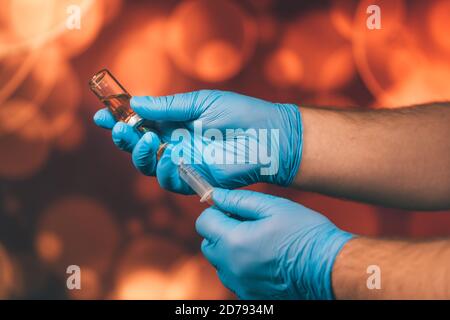 Un medico con guanti blu aspira una fiala in una siringa. Vaccino medico contro il concetto di influenza coronavirus flacone di iniezione per vetro medico Foto Stock