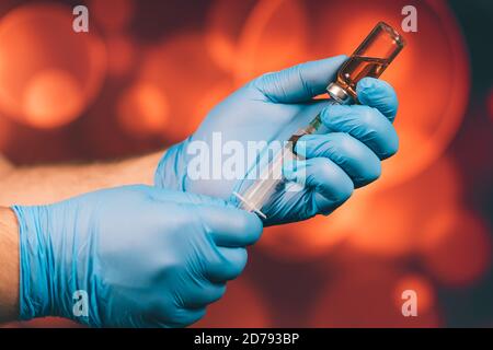 Un medico con guanti blu aspira una fiala in una siringa. Vaccino medico contro il concetto di influenza coronavirus flacone di iniezione per vetro medico Foto Stock