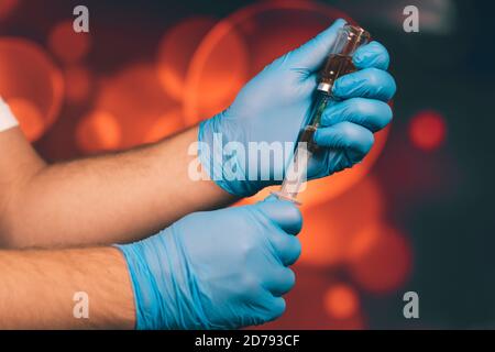 Un medico con guanti blu aspira una fiala in una siringa. Vaccino medico contro il concetto di influenza coronavirus flacone di iniezione per vetro medico Foto Stock