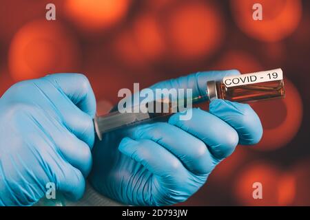 Un medico con guanti blu aspira una fiala in una siringa. Vaccino medico contro il concetto di influenza coronavirus flacone di iniezione per vetro medico Foto Stock
