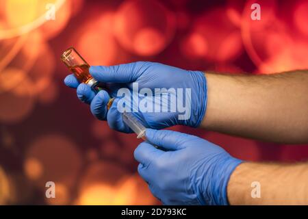 Un medico con guanti blu aspira una fiala in una siringa. Vaccino medico contro il concetto di influenza coronavirus flacone di iniezione per vetro medico Foto Stock