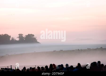 Il sole comincia a sorgere sui campi che circondano Stonehenge. Il Solstizio d'Estate a Stonehenge. Foto Stock