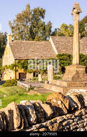 Luce serale sul memoriale di guerra in St Barnaba Churchyard e un cottage in pietra tradizionale nel villaggio di Cotswold di Snowshill, Gloucestershire UK Foto Stock