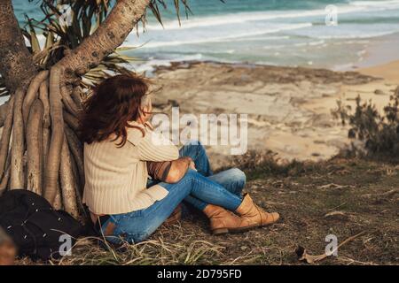 Felice coppia di mezza età in amore seduto sotto l'albero con vista ocen, abbraccio, sorriso e guardare l'oceano. Foto Stock