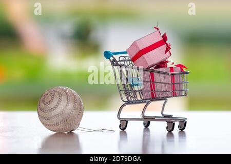 Palla di Natale e carrello con regali su sfondo sfocato, concetto di shopping di Natale, coco su un carrello Foto Stock