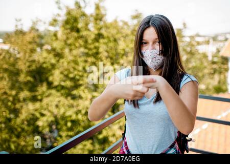 Ragazza seria disinfettando le mani e indossando la maschera personale protettiva per il viso Foto Stock