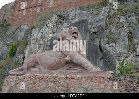 Una statua di un leone fatto di arenaria rosa nella fortezza o cittadella a Belfort, Francia. Sullo sfondo si trova una parete di roccia di colore contrastante. Foto Stock