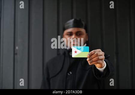 Uomo africano indossare durag nero tenere bandiera Gibuti a mano isolato sfondo scuro. Foto Stock