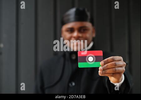 Uomo africano indossare durag nero tenere Malawi bandiera a mano isolato sfondo scuro. Foto Stock