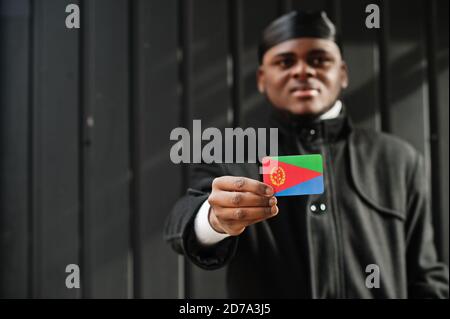 Uomo africano indossare durag nero tenere bandiera Eritrea a portata di mano isolato sfondo scuro. Foto Stock