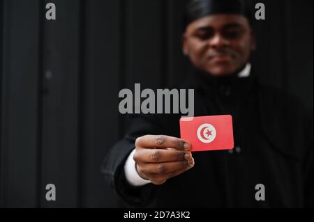 Uomo africano indossare durag nero tenere la bandiera tunisina a mano isolato sfondo scuro. Foto Stock