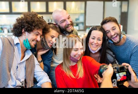 gruppo sorridente di persone caucasiche che indossano una maschera protettiva per il viso in posa per una foto insieme di fronte a una fotocamera reflex fotografo. selfie. Foto Stock