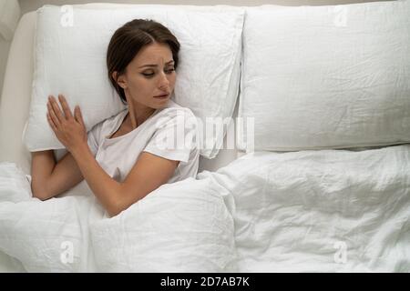 Vista dall'alto della donna triste che si trova a letto da sola, guardando da parte un cuscino vuoto, depresso, sentendosi solitario dopo il litigio con il suo ragazzo o divorzio, Foto Stock