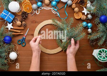 Processo passo-passo di fare una corona di albero di Natale a casa da rami di abete rosso, arance e palle di Natale nei colori argento e blu del Foto Stock