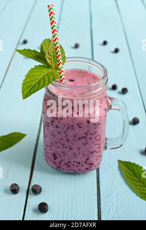 Frullato di mirtillo con menta in vasetto di muratore con paglia su fondo di legno. Foto Stock