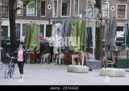 Un uomo che indossa una maschera protettiva spinge il suo poass di bicicletta oltre la terrazza chiusa alla Leidseplein in mezzo alla pandemia di Coronavirus il 21 ottobre 2020 ad Amsterdam, Paesi Bassi. La città di Amsterdam ha ora uno dei peggiori tassi di infezione del Covid-19 in Europa, oggi il numero di casi segnalati di COVID-19 continua ad aumentare in tutte le regioni dei Paesi Bassi con 8,764 nuovi casi in 24 ore secondo l'ultima indagine dell'istituto di sanità pubblica (RIVM). Il primo ministro olandese Mark Rutte ha annunciato la scorsa settimana nuove misure più severe per cercare di controllare nuove infezioni, tutti i caffè, bar e ristoranti Foto Stock