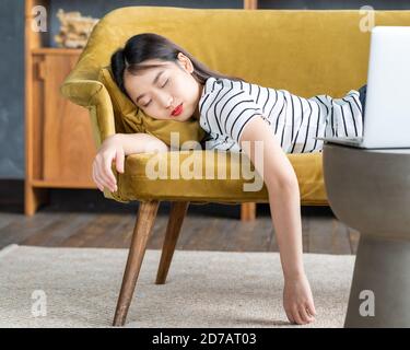 La giovane ragazza asiatica si addormentò sul divano davanti a un laptop. La donna carina è annoiata, stanca o overworked. Foto Stock