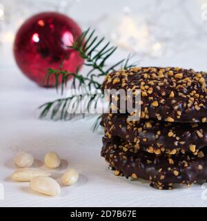 Avvento e umore natalizio, Elisenlebkuchen con glassa al cioccolato e nocciole, su un tavolo di legno bianco sullo sfondo una palla rossa di natale Foto Stock