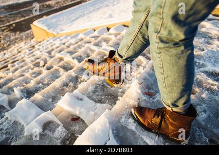 L'inverno è in arrivo. Stivali femmina su superficie di ghiaccio con scivolone ruvido. Una donna in pelle marrone scarpe discende la scala di ghiaccio scivoloso. Foto Stock