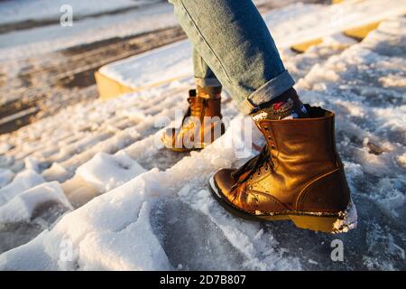 L'inverno è in arrivo. Stivali femmina su superficie di ghiaccio con scivolone ruvido. Una donna in pelle marrone scarpe discende la scala di ghiaccio scivoloso. Foto Stock