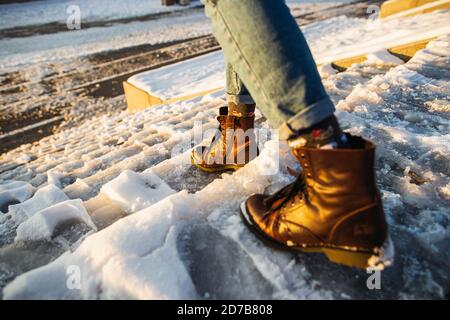 L'inverno è in arrivo. Stivali femmina su superficie di ghiaccio con scivolone ruvido. Una donna in pelle marrone scarpe discende la scala di ghiaccio scivoloso. Foto Stock